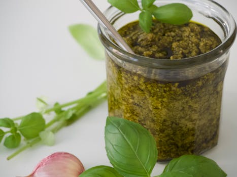 A detailed view of fresh homemade basil pesto with garlic and leaves.