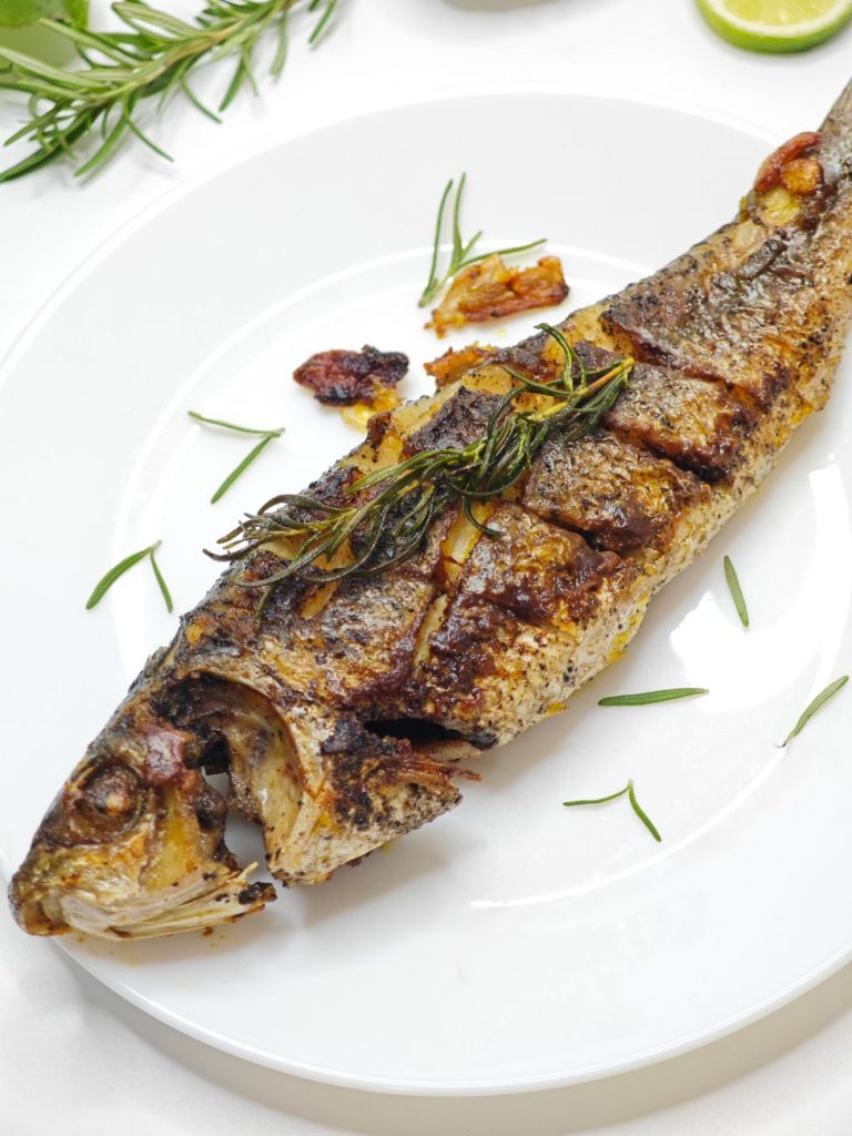 grilled whole fish with herbs on white plate