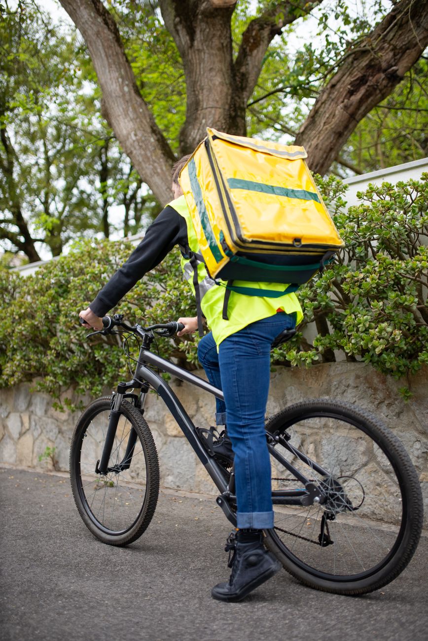 a person in black long sleeve shirt carrying a yellow and green backpack while riding a bicycle