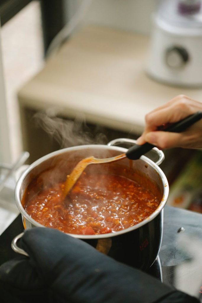 crop unrecognizable chef stirring bolognese sauce in saucepan