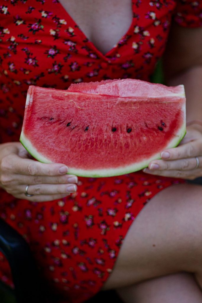 a woman in a red dress holding a slice of watermelon