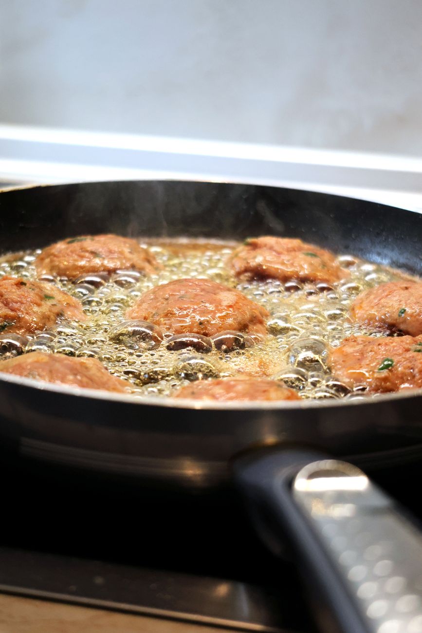 greek style fried meatballs cooking in pan