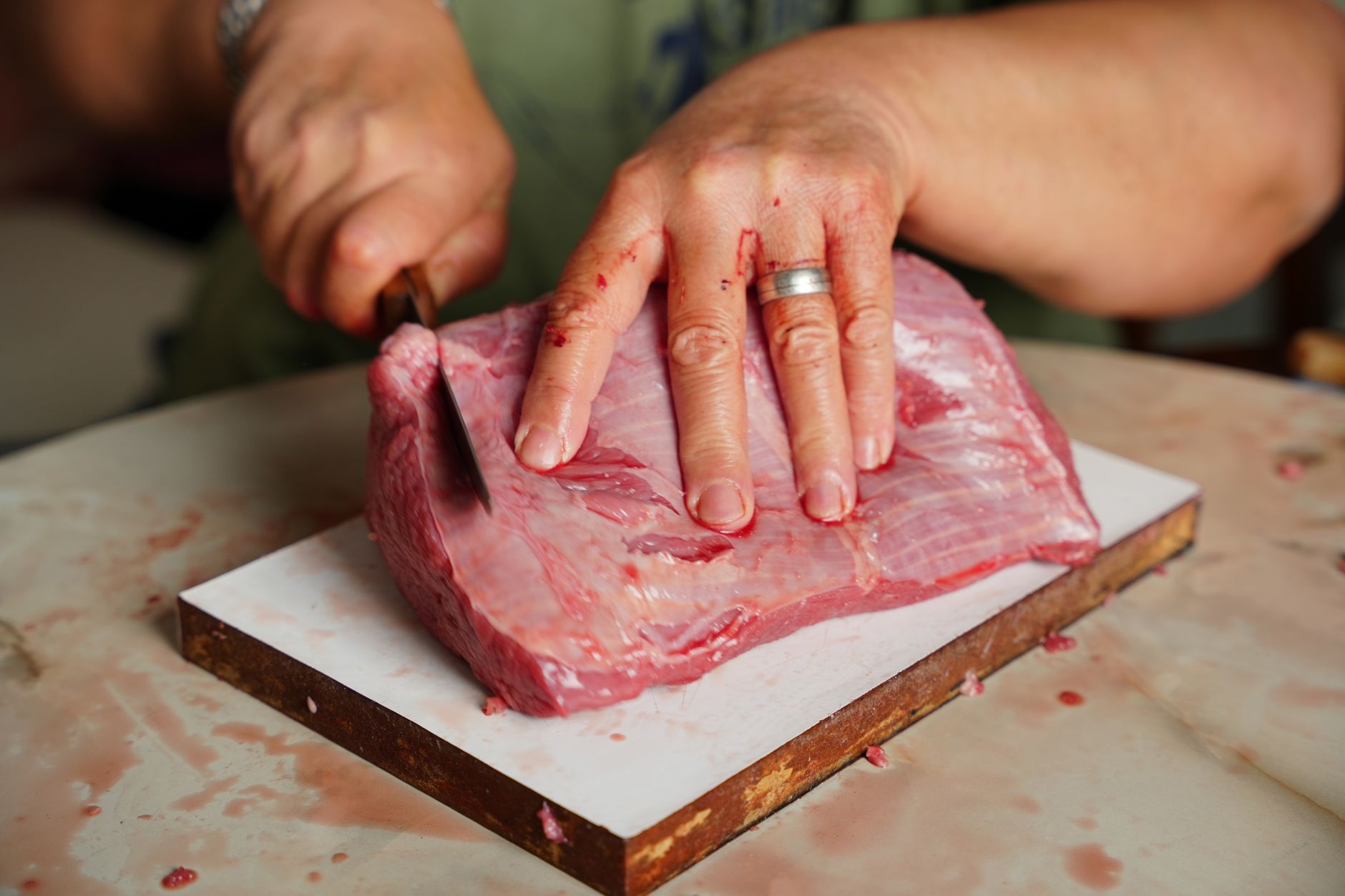 close up of hands cutting raw meat on a board