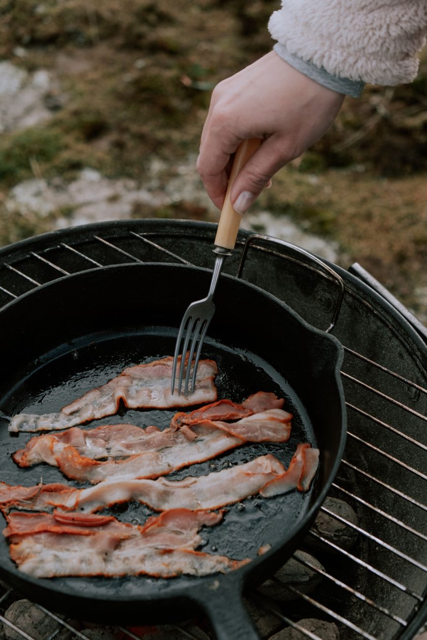 a hand cooking strips of meat on a frying pan