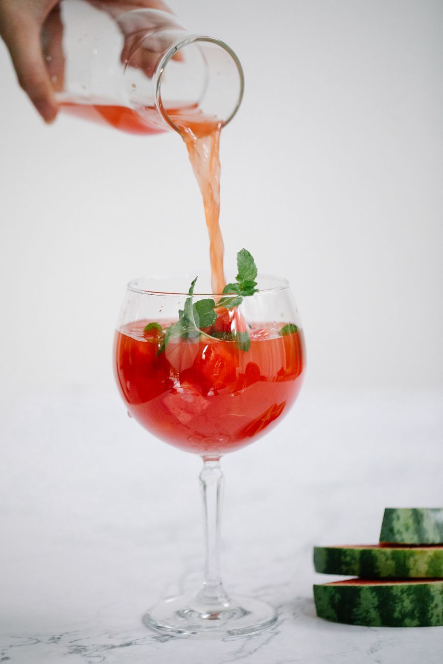 person pouring red cocktail drink in a wine glass